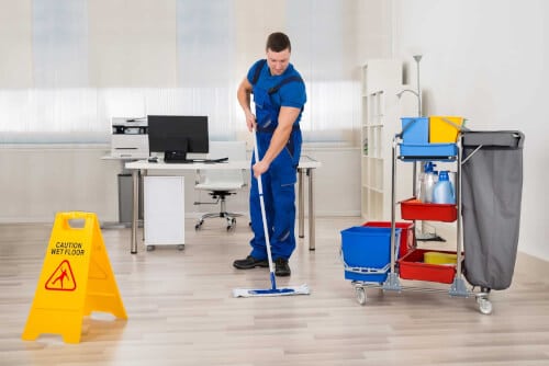Addetto alle pulizie che pulisce il pavimento di una stanza d'ufficio con la sua attrezzatura
