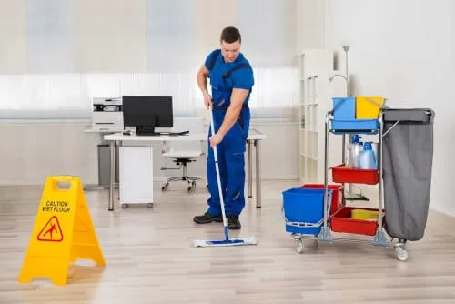 Addetto alle pulizie che pulisce il pavimento di una stanza d'ufficio con la sua attrezzatura Addetto alle pulizie che pulisce il pavimento di una stanza d'ufficio con la sua attrezzatura