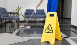 Addetto alle pulizie che pulisce il pavimento con un cartello giallo